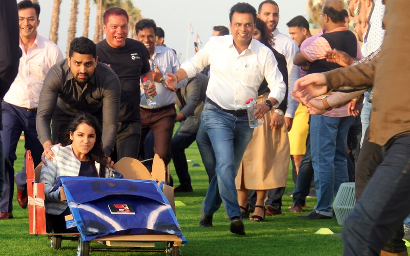 A team pushing their home built cart along the grass while the group cheers them on