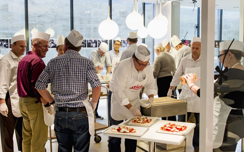 A team in chef hats and aprons finishing their pizzas at the work tables