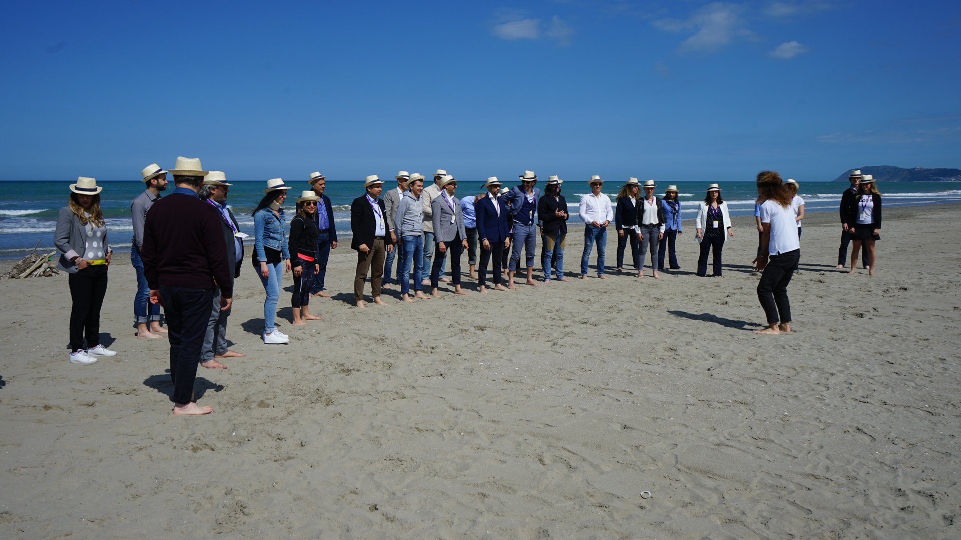 A large group standing in a circle on the beach during a team building day