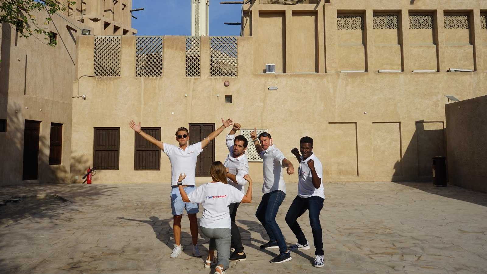 A team striking a pose in a courtyard of Al Fahidi, wind towers and a minaret behind