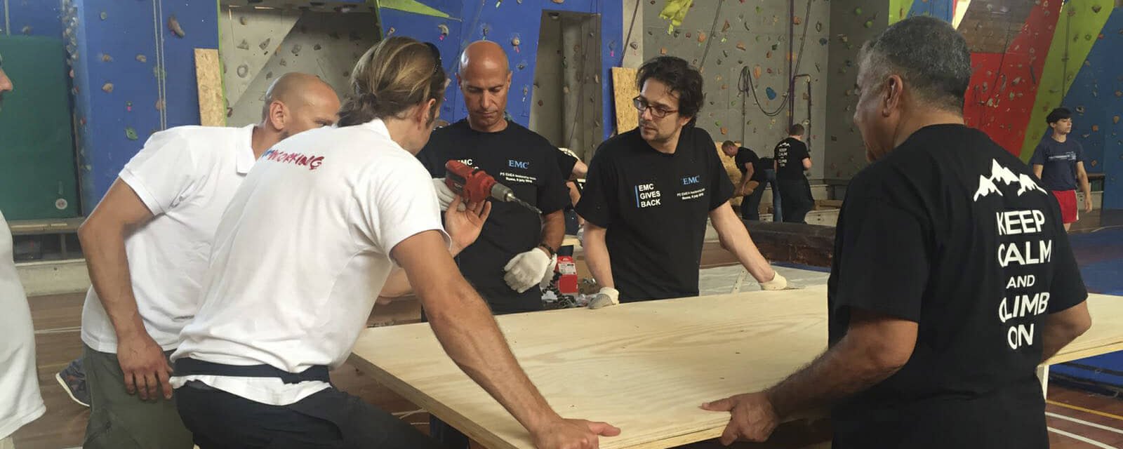 A team carrying a wooden panel together at the climbing wall during a social build