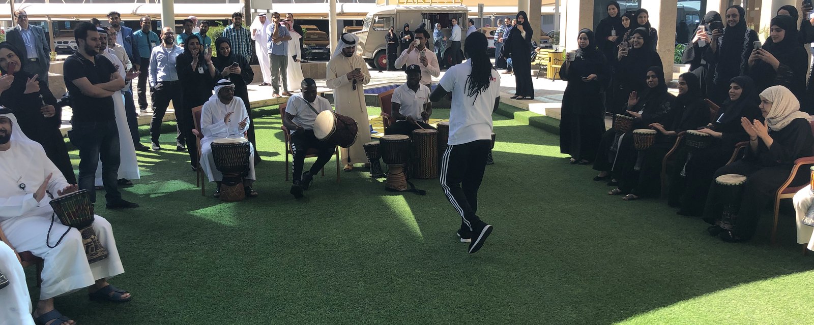 Participants in kandura and abaya playing hand drums together outdoors in Ajman